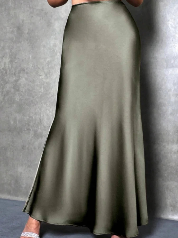 Olive high-shine flared maxi skirt worn with silver heeled sandals against gray backdrop