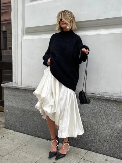 Full-length view of woman in flowing ivory satin skirt paired with oversized black knit sweater