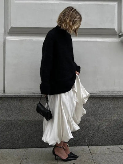 Back view of woman in black sweater and ivory satin maxi skirt carrying a black chain bag