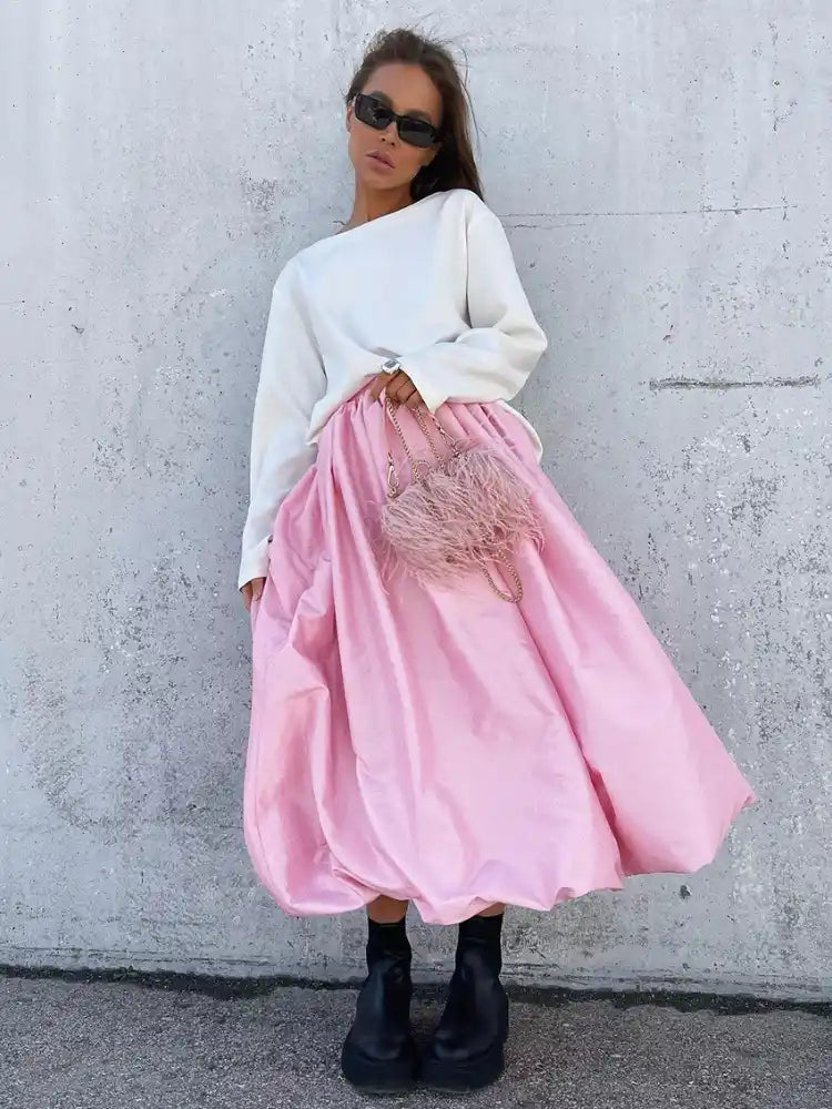 Woman wearing pink balloon-hem midi satin skirt with white sweatshirt and black ankle boots