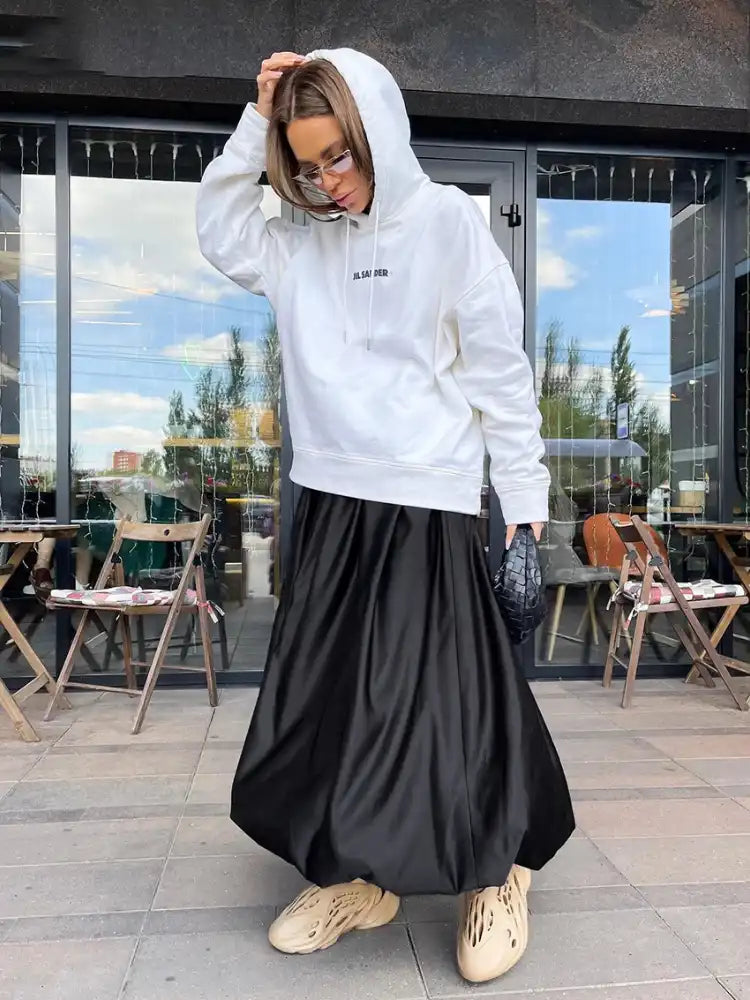 Woman wearing a black balloon-hem maxi satin skirt with a white Jil Sander hoodie outdoors