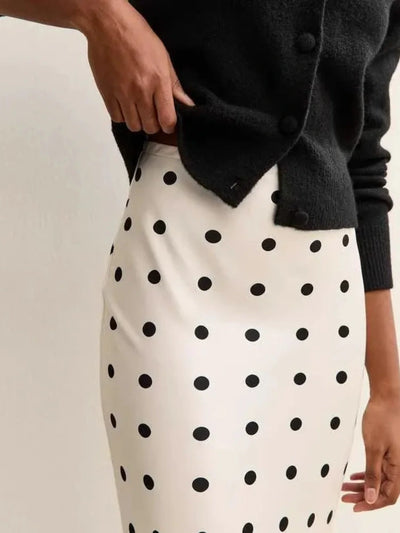 Close-up of an ivory polka dot satin midi skirt with black dots, tucked under a black cardigan