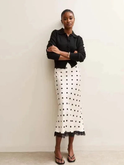 Model wearing an ivory polka dot midi skirt with a black cardigan, arms crossed, front view