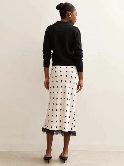 Back view of model in ivory polka dot midi skirt with black lace hem and black knit top