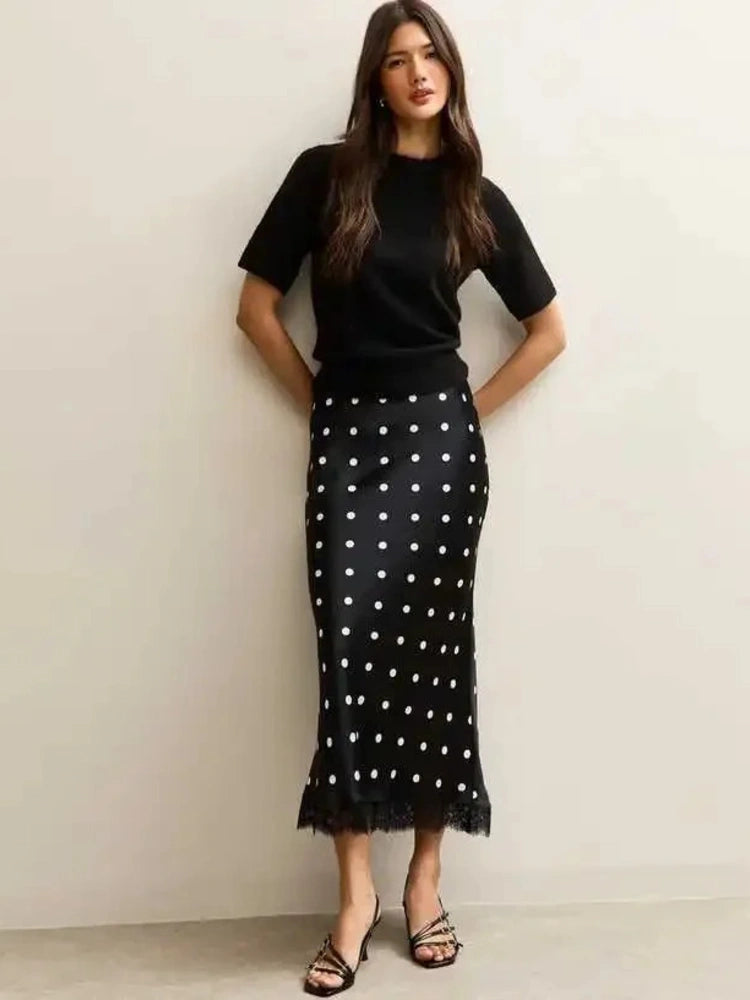 Woman wearing black polka dot midi skirt with lace hem and black knit top, front view