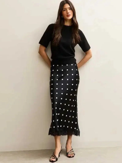 Woman wearing black polka dot midi skirt with lace hem and black knit top, front view