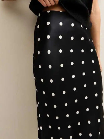 Close-up of black satin-finish midi skirt with white polka dots and clean waistband