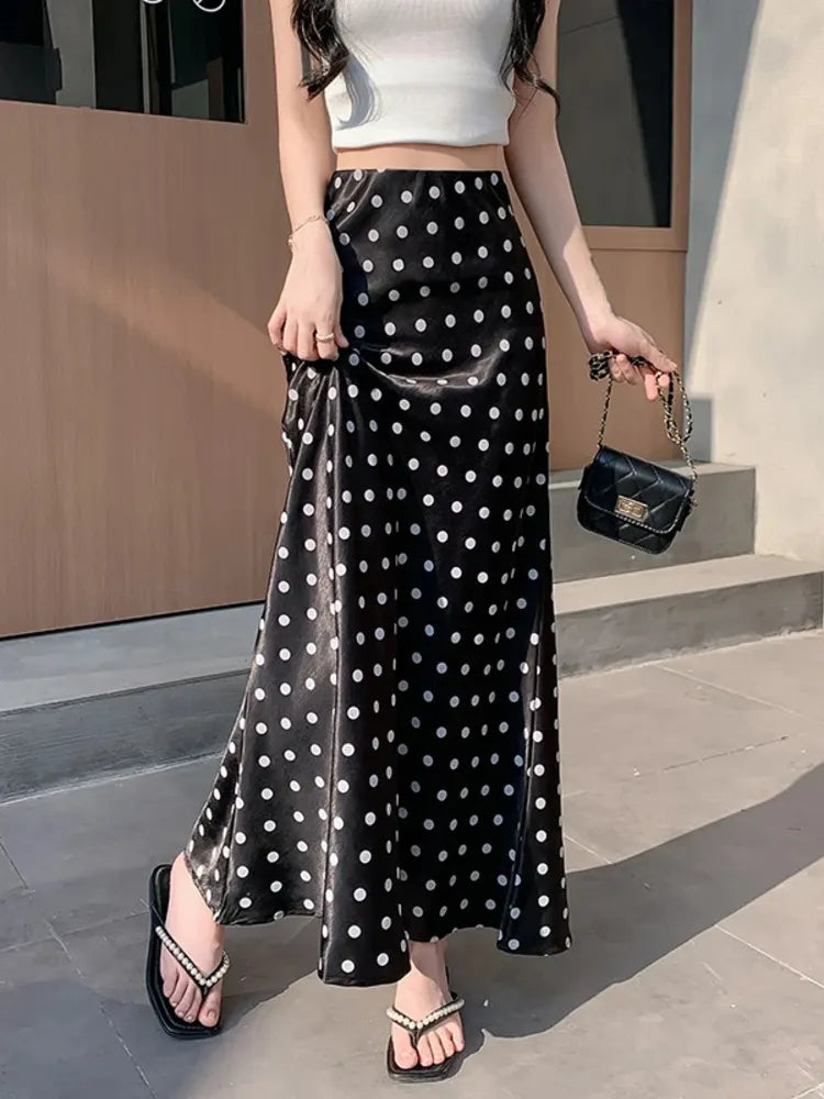Woman wearing black and white polka dot mermaid maxi skirt with white crop top and black bag, side view showing slit