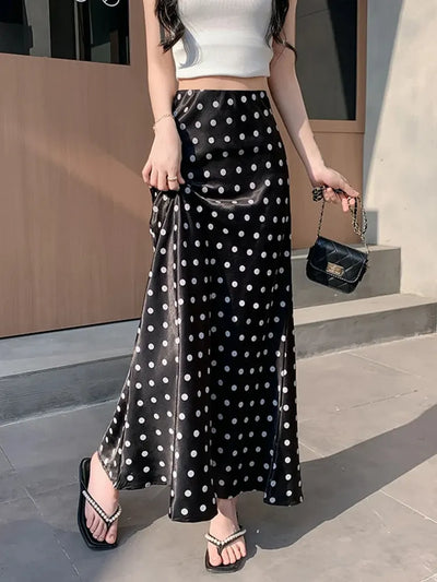 Woman wearing black and white polka dot mermaid maxi skirt with white crop top and black bag, side view showing slit