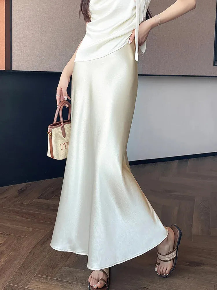 Ivory mermaid-cut maxi satin skirt on woman with woven tote and sandals