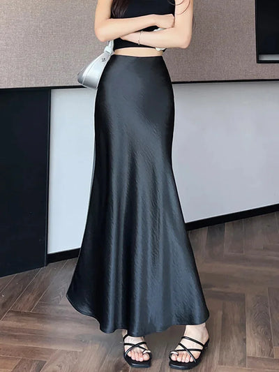 Woman wearing a black crinkled satin fishtail maxi skirt with a black crop top and strappy sandals, arms crossed