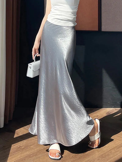 Full-length view of a silver crinkled satin maxi skirt with flared fishtail hem in natural sunlight