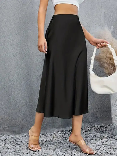 Front view of a black satin midi skirt styled with a white crop top and clear sandals outdoors