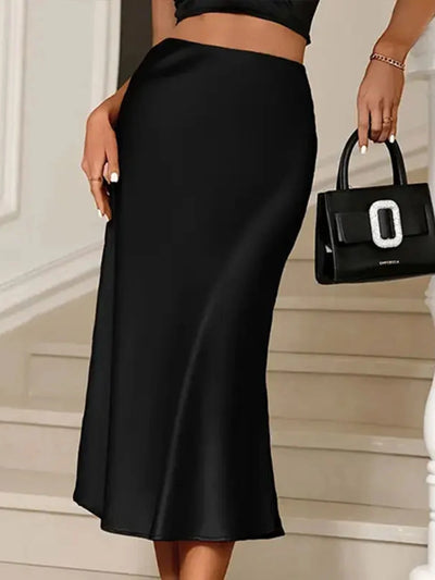 Close side view of a black high-waist satin midi skirt paired with a crop top and structured handbag