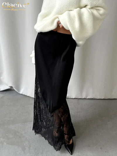 Side view of black satin midi skirt with asymmetric floral lace panel and scalloped hem, styled with cream knit sweater and black pointed-toe heels