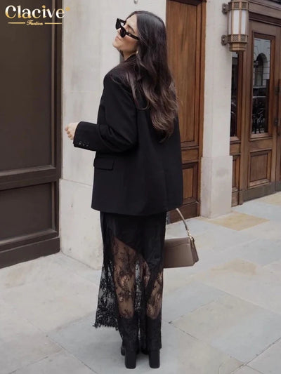 Woman wearing black lace-hem midi skirt and oversized black blazer with ankle boots on a city street, back view
