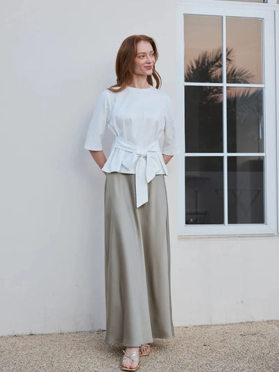 Woman wearing sage green satin maxi skirt with white tie-waist top and gold sandals outdoors