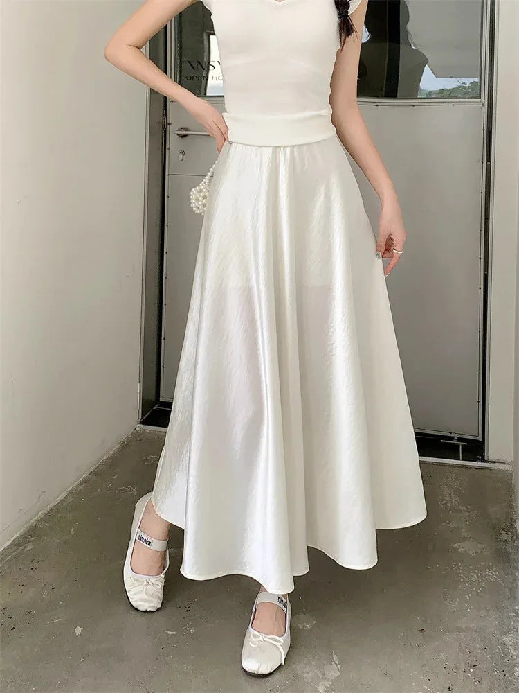 Woman wearing a white crinkled satin A-line maxi skirt with a white tank top and ballet flats