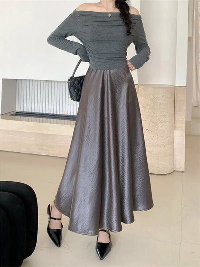 Woman standing in a crinkled gray satin A-line midi skirt with off-shoulder gray top and black heels