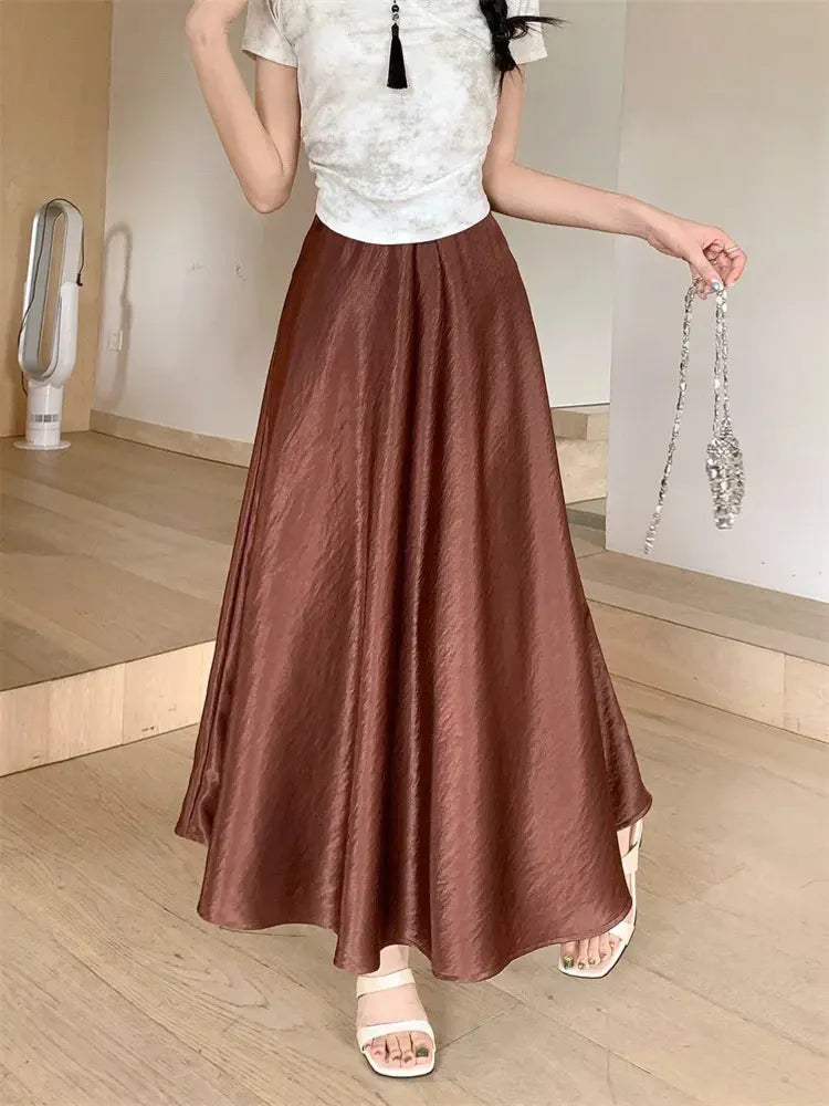 Woman wearing a brown crinkled satin flared midi skirt with white printed top and sandals