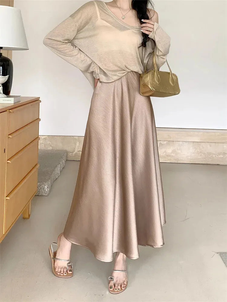 Champagne satin A-line maxi skirt styled with sheer long-sleeve top, gold bag, and silver sandals