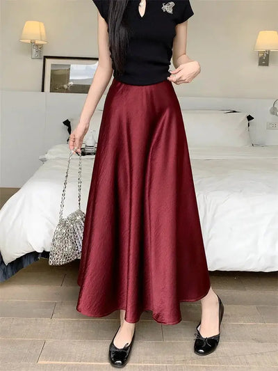 Woman standing in a burgundy high-waist A-line midi satin skirt, black tee, and ballet flats