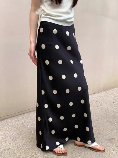 Woman wearing a black maxi satin skirt with large cream polka dots and white sandals, side view