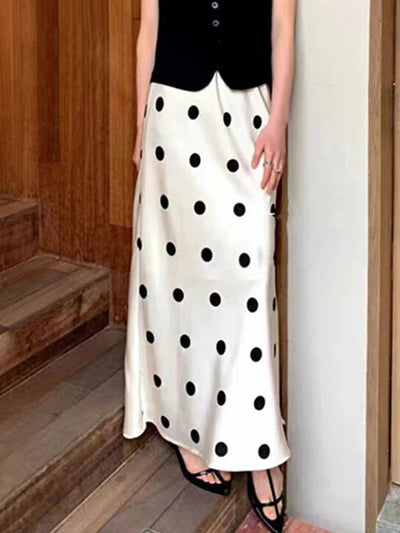 Woman wearing ivory polka dot maxi satin skirt paired with a black button vest and strappy heels