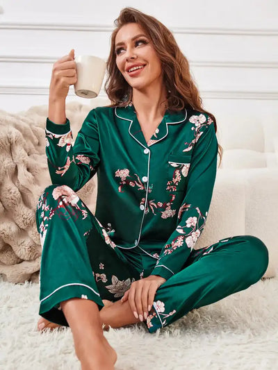 Woman sitting cross-legged on floor wearing green floral crane satin pajama set holding white mug