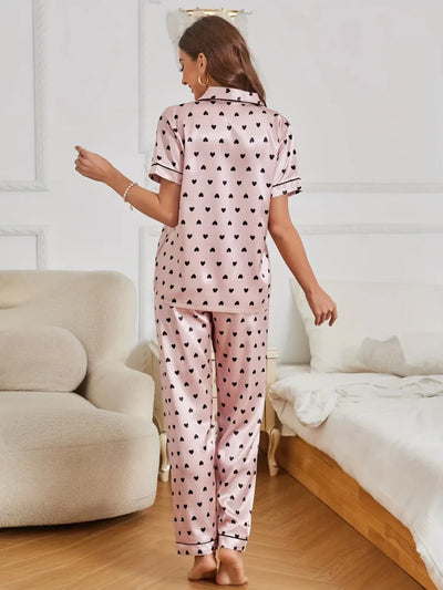 Back view of woman standing in pink satin heart print short sleeve pajama shirt and long pants