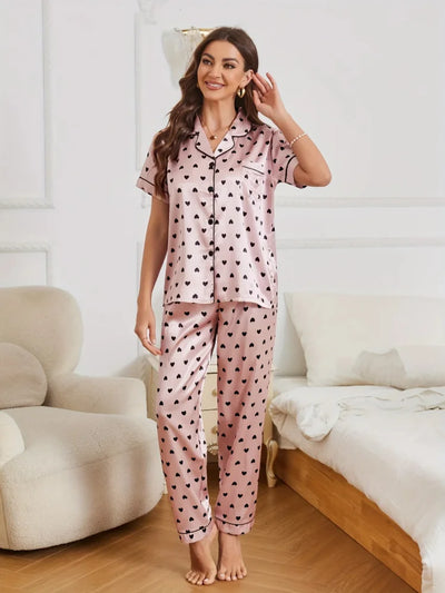 Woman smiling and standing in pink satin heart print pajama set with long pants, full length front view