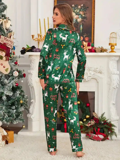 Back view of woman in green satin Christmas pajama set showing full-length pants and all-over holiday print near fireplace