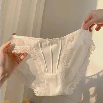 Two hands holding white pleated satin panties with wide lace trim and small bow detail at waistband