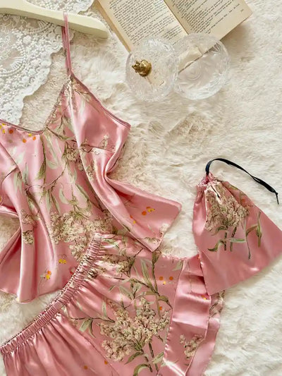 Flat lay of pink floral satin cami top, ruffled shorts, and matching drawstring pouch with open book