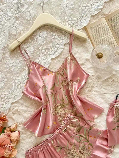 Pink satin cami top with floral print on hanger beside ruffled shorts on white lace background
