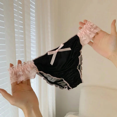 Black satin panties with pink lace ruffle sides held up against white background