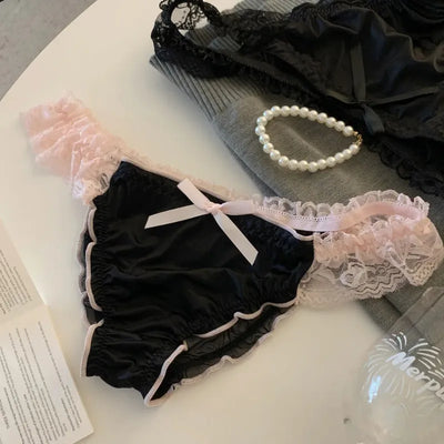 Black satin panties with pink lace ruffle trim and white bow on round surface flat lay