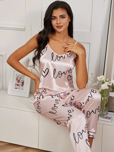Woman wearing blush pink satin cami pajama set with black love script print and long pants
