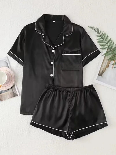 Flat lay of black satin button-down pajama shirt and shorts set with white contrast piping