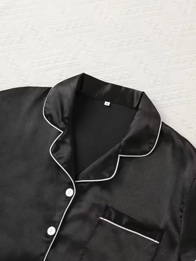Close-up of black satin pajama shirt collar and chest pocket with white piping detail