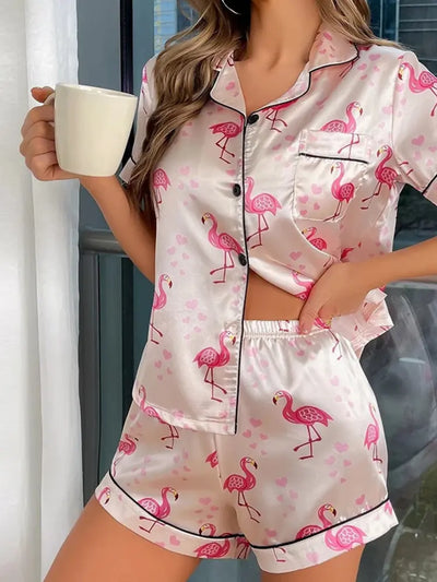 Woman in blush pink satin flamingo print pajama set holding a white coffee mug near a window