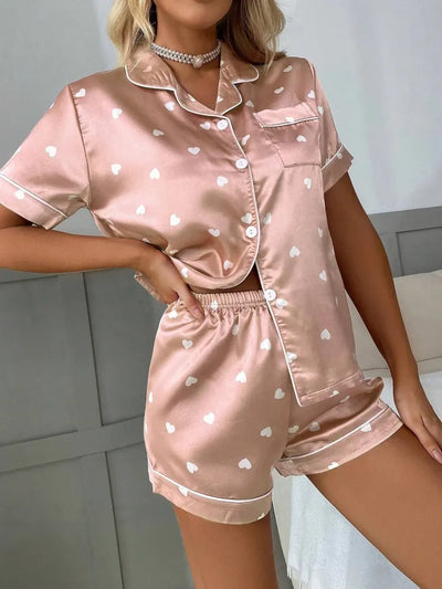 Blush pink satin pajama set with white heart print, button-front top and matching shorts, front view standing pose