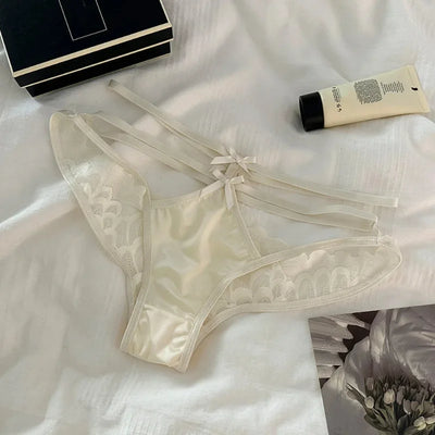 Ivory satin and scalloped lace panties with ribbon bow ties flat lay on white fabric