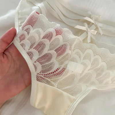 Close-up of sheer floral scalloped lace panel on ivory satin panties held by hand