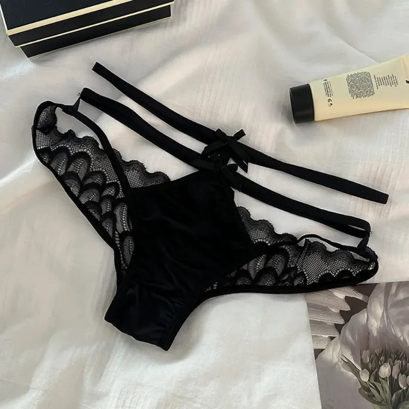 Black satin panties with scalloped lace sides, double-strap waistband, and small bow at center back, flat lay on white fabric
