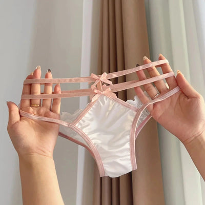 Two hands holding white satin panties with blush pink multi-strap bow waistband and lace trim