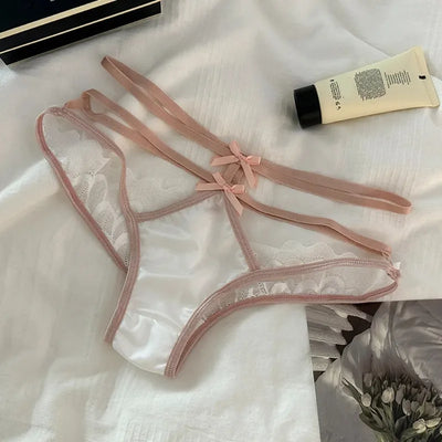 White satin bow panties with blush elastic straps and lace trim laid flat on white fabric