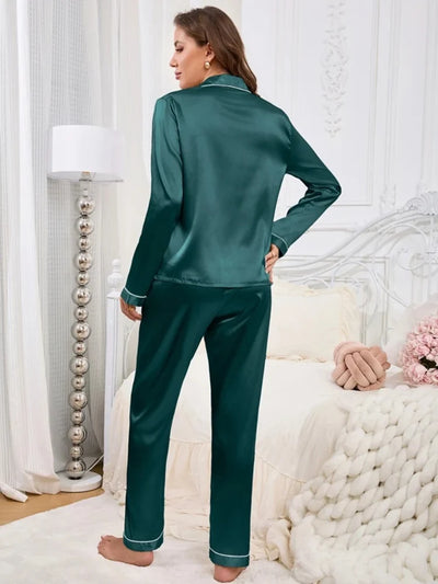 Back view of woman standing in teal satin long-sleeve pajama set with white contrast piping on hem and cuffs