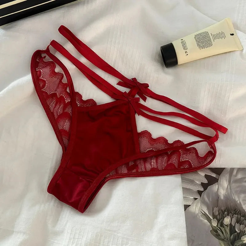 Red lace-trim strappy satin panties with scalloped panels and ribbon bow ties at hip, flat lay on white fabric