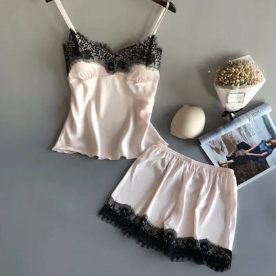 Blush satin cami and shorts pajama set with black lace trim, flat lay on gray surface